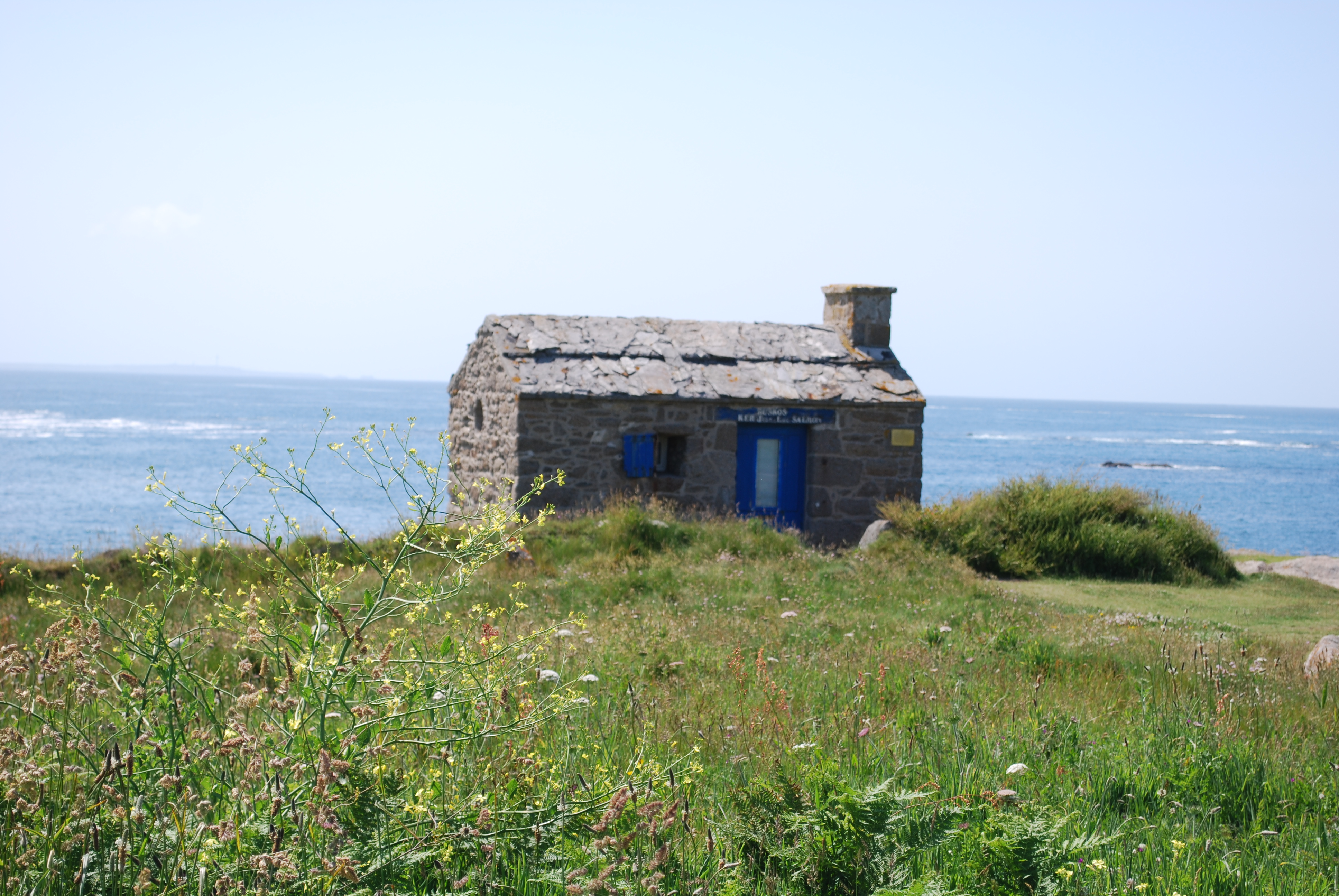 Phare breton illuminé au coucher du soleil avec la mer calme et ciel pastel